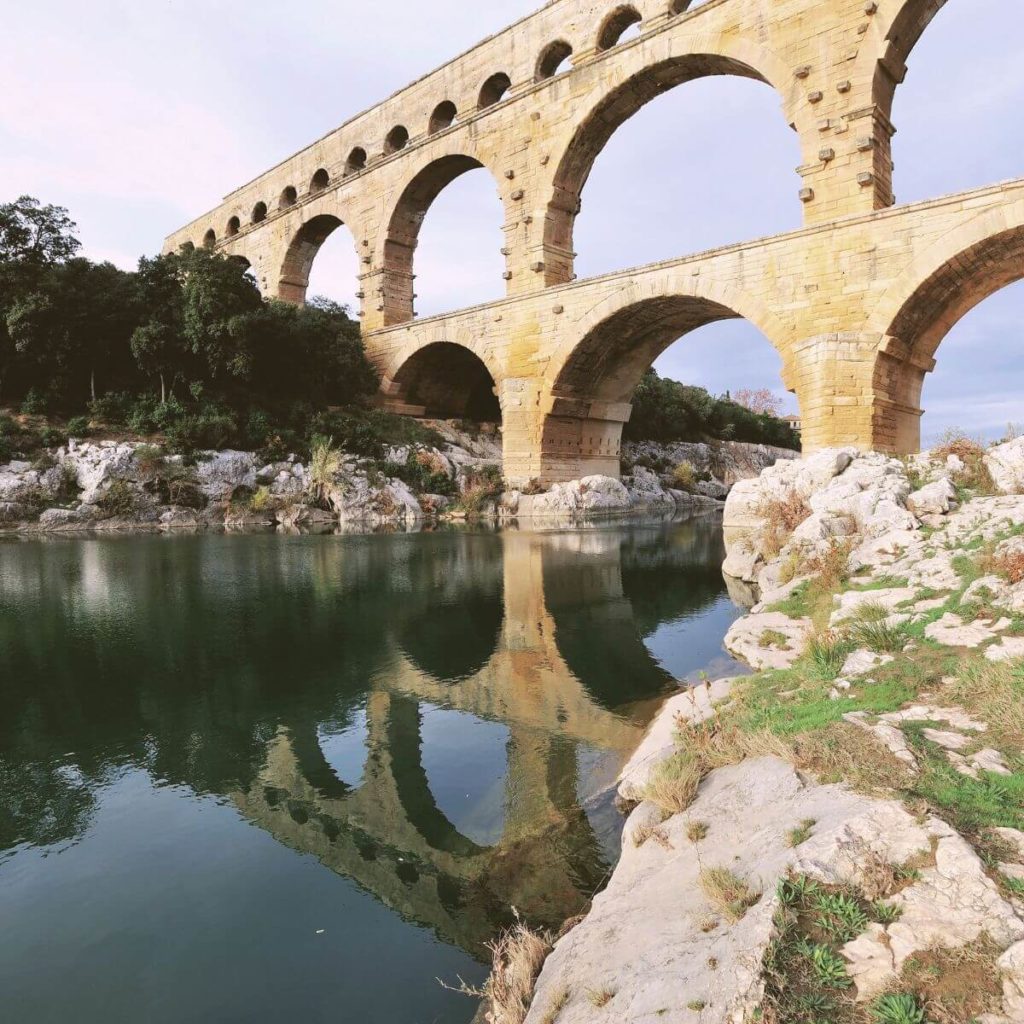 Photo of the Pont du Garde Roman aqueduct reflecting in the river below it.