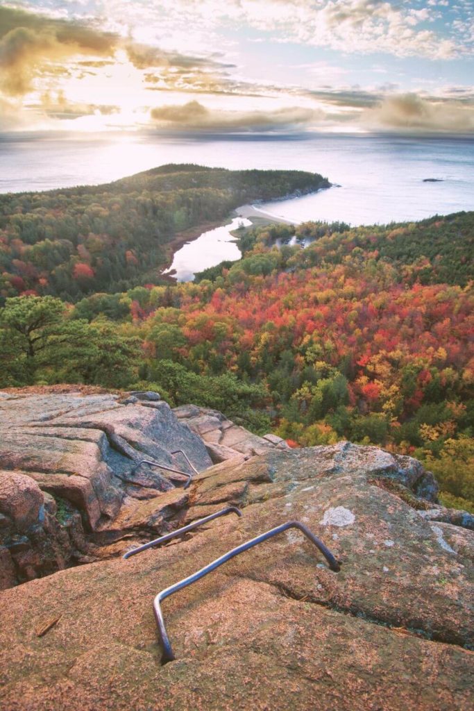 Aerial view of the ocean and forest below the summit of Beehive Trail in Acadia National Park with iron rungs running up the rock ascent.
