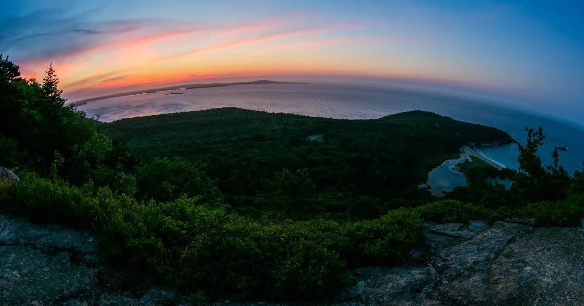 Photo of the view from the top of the Beehive Trail in Acadia National Park at sunrise, with the Gulf of Maine and Sand Beach below.