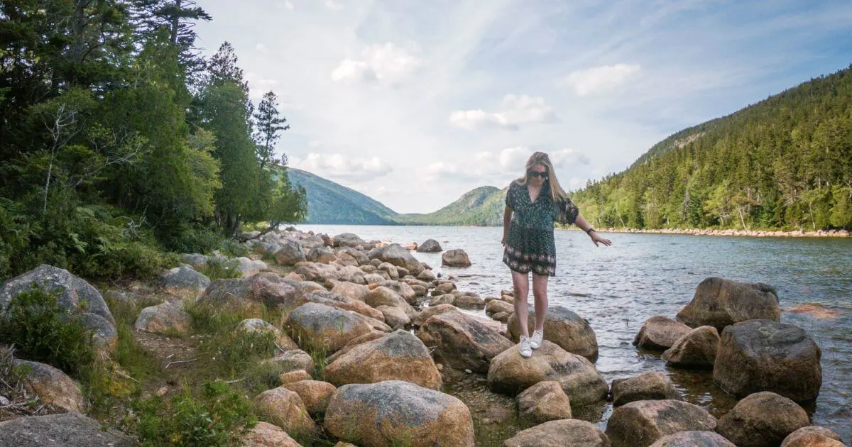 Photo of a woman walking across large rocks that line the Jordan Pond Trail in Maine's Acadia National Park.