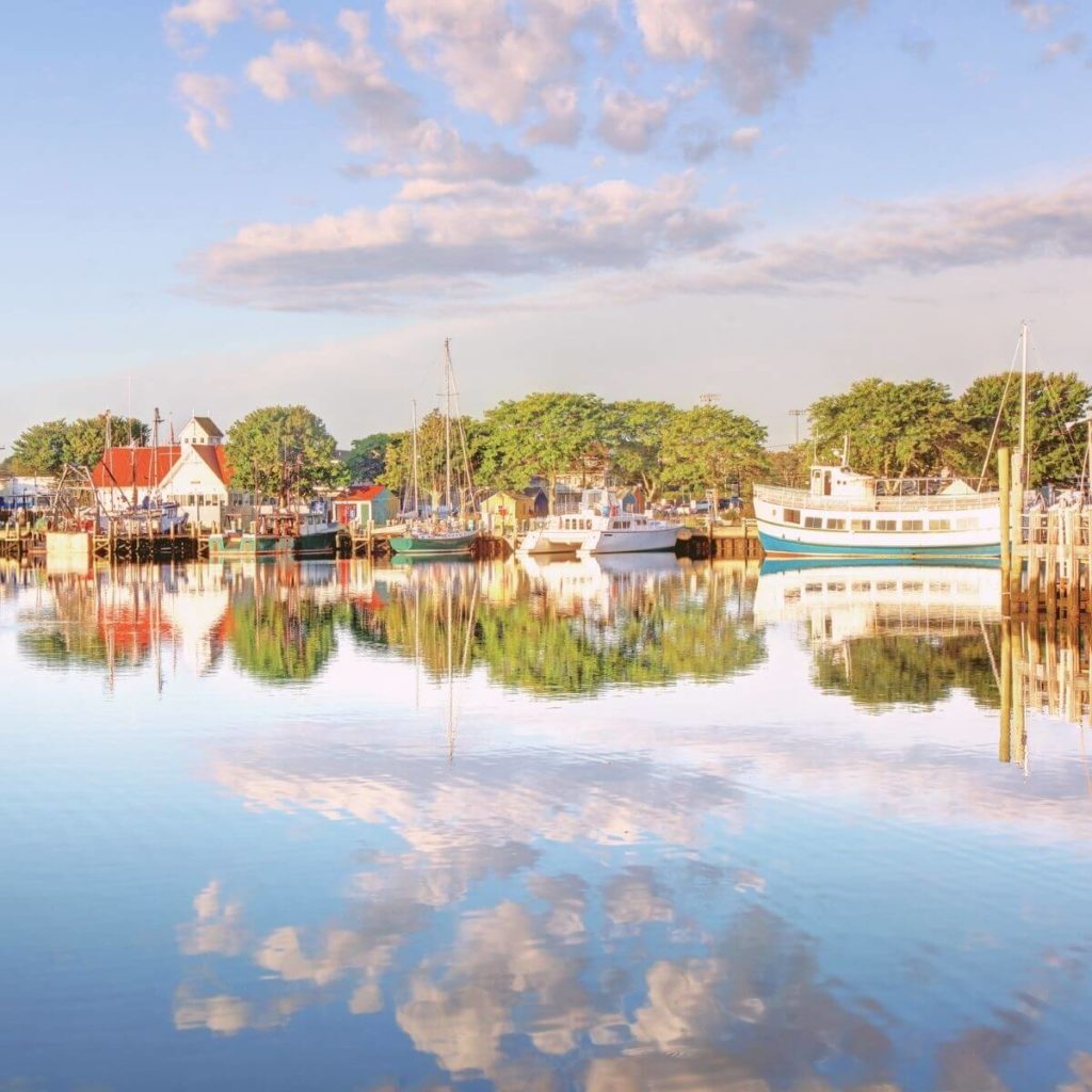Photo of Hyannis Harbor in Barnstable, MA with houses, boats, and clouds reflecting in the water.