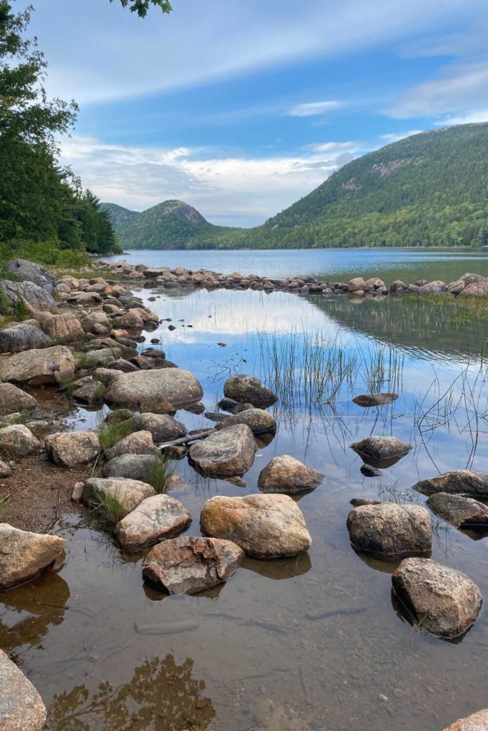 Photo of Jordan Pond with reflections of nearby mountains, trees, and rocks in the water.