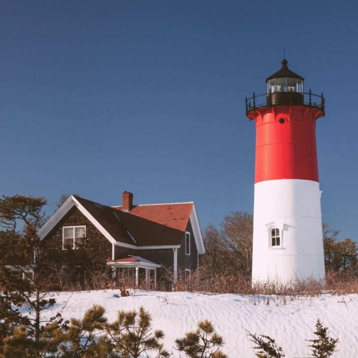 Photo of Nauset Lighthouse in Eastham, MA with a small cottage next to it and powdery white sand in the foreground.