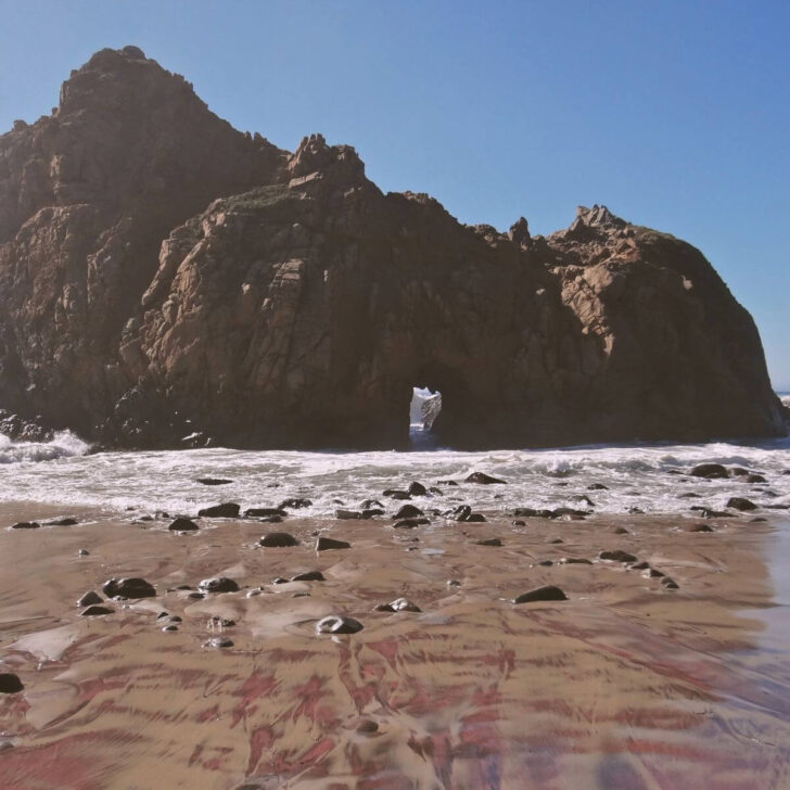 Photo of Pfeiffer Beach in Big Sur, CA, with purple striped sand and Keyhole Rock in the background.