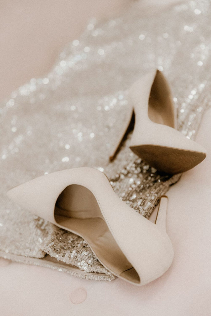 Closeup of a pair of off white high heels and a silver sequin dress.
