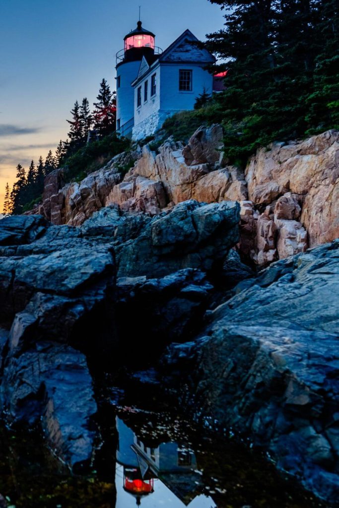 Photo of Bass Harbor Head Lighthouse Trail at sunrise with the lighthouse reflecting in a puddle.