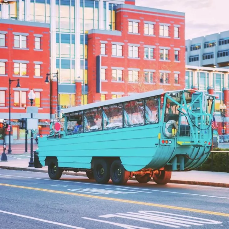 Photo of an aqua Boston Duck Tour vehicle driving on the street.