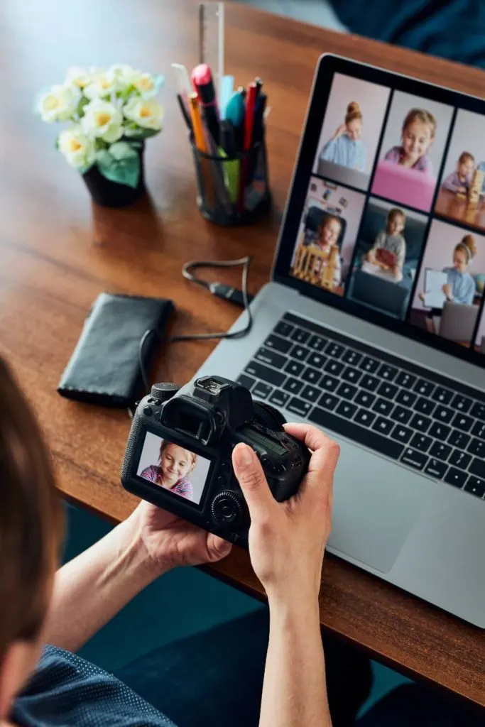 Photo of a person looking at the back of a camera hooked up to a laptop with other photo proofs on display.