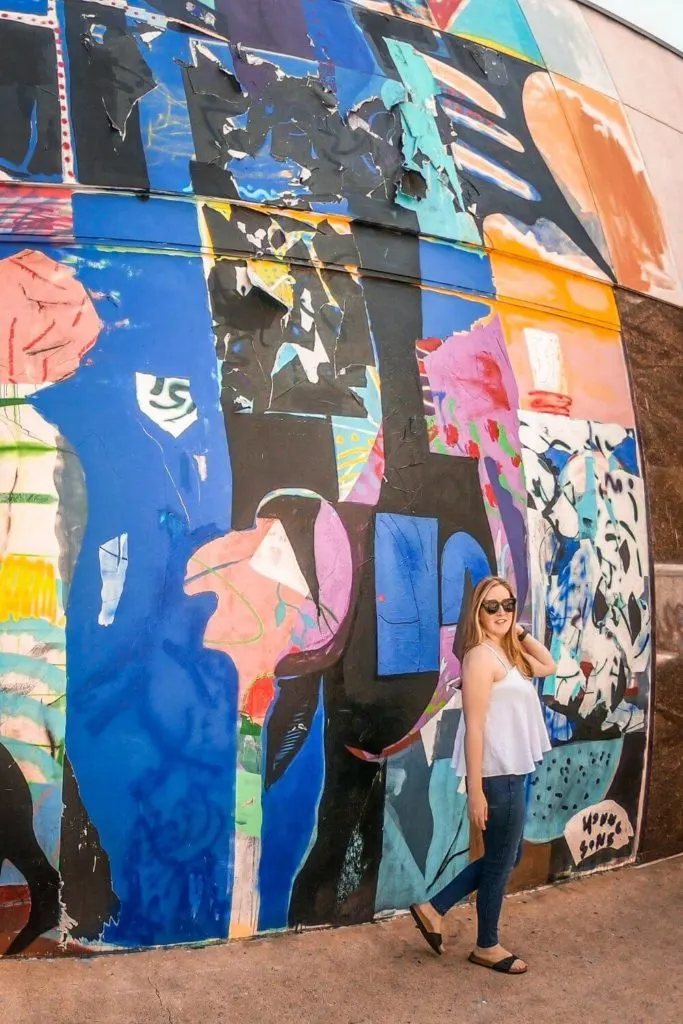 Photo of a woman posing in front of a large street art mural.