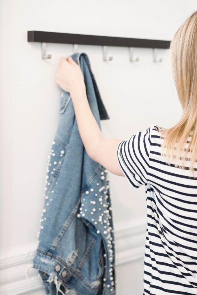 Closeup of a woman in a black and white striped t-shirt grabbing a pearl-embellished denim jacket.