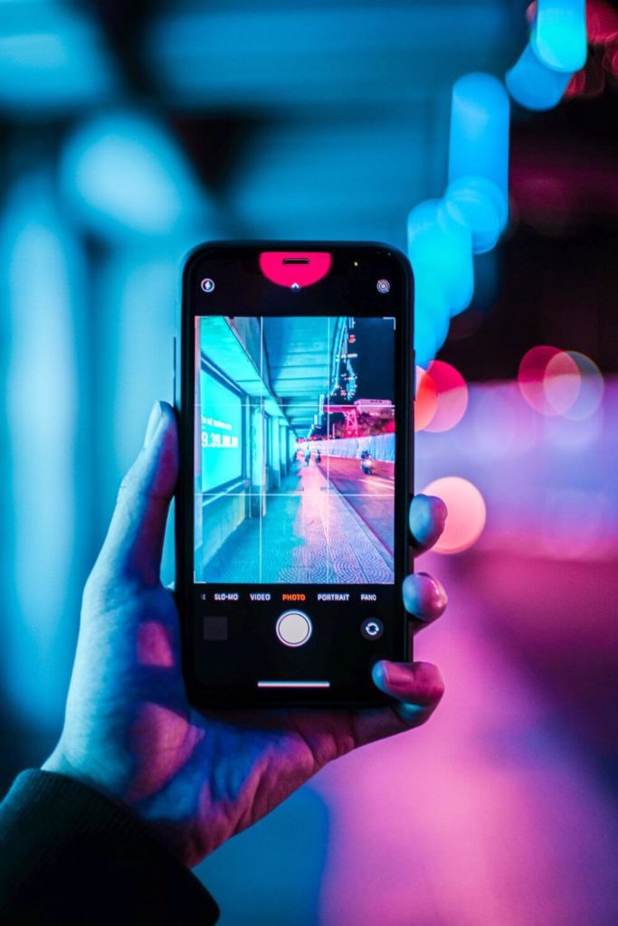 Photo of person taking a photo of a pink and blue neon lit hallway at night.