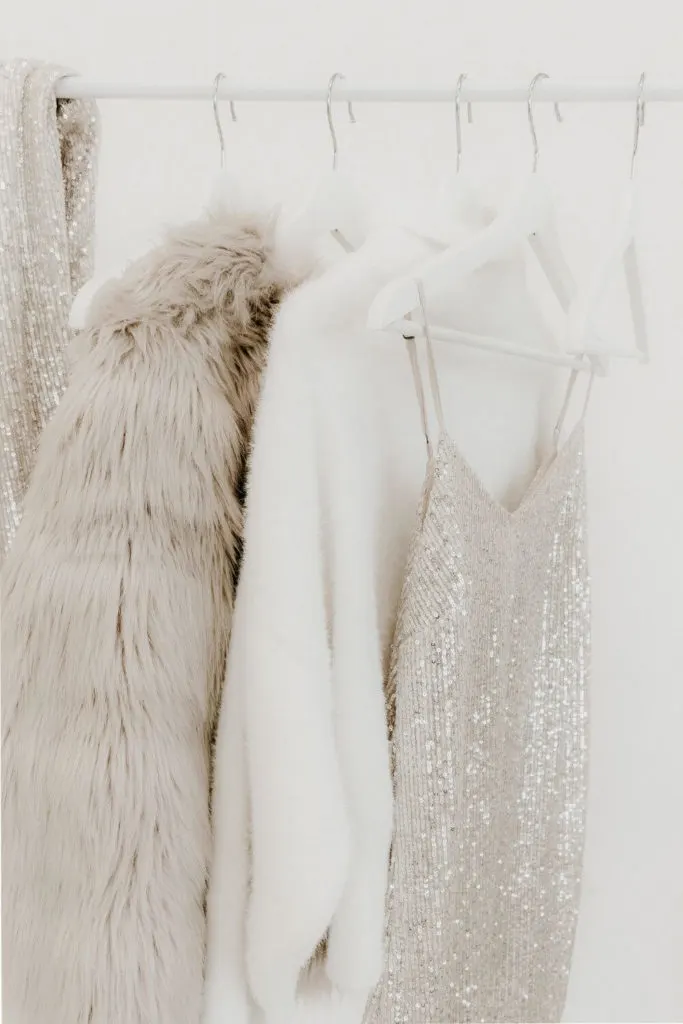 Closeup of a clothing rack with a faux fur coat, fuzzy white sweater, silver sequin dress, and other Vegas outfits.