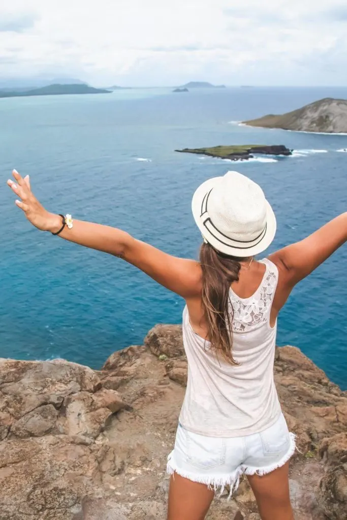 Photo of a woman wearing a sun hat, tank top, and shorts, posing at the top of a hike in Hawaii.