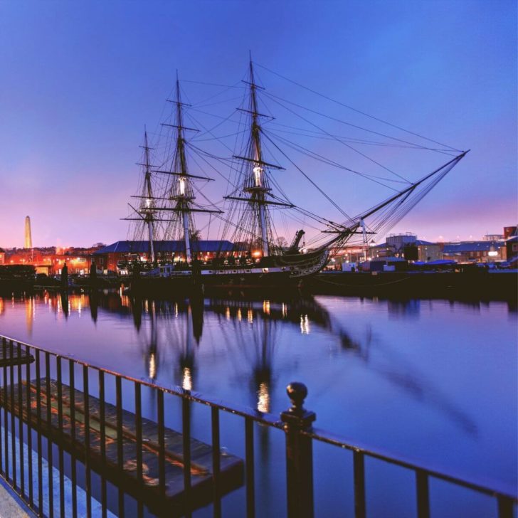 Photo of the USS Constitution at night, reflecting in the water.