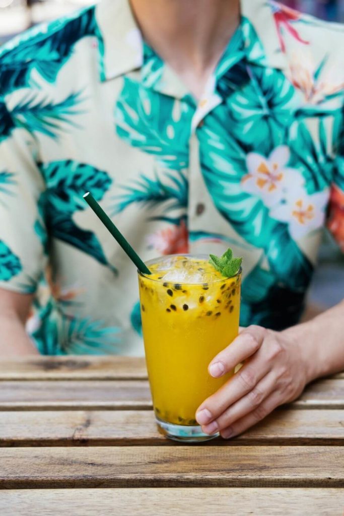 Closeup of a man wearing an aloha shirt will drinking lilikoi (passionfruit) juice.