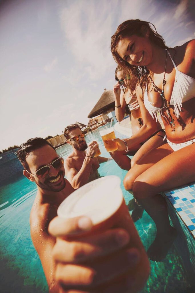 Photo of young adults hanging out at a pool with beers in their hand.