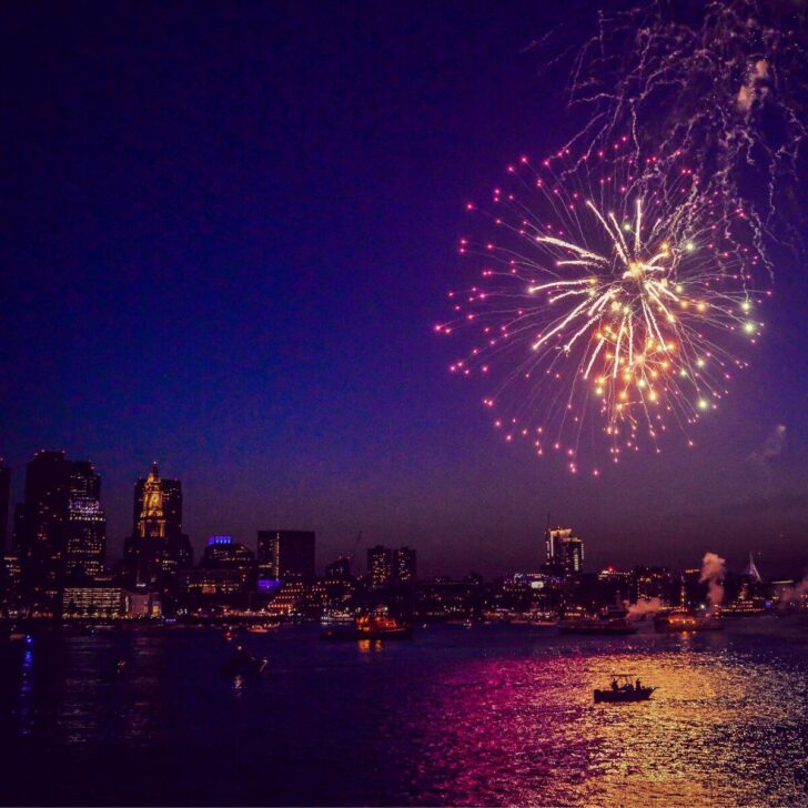 Photo of a firework exploding over the Charles River with a silhouette of a boat in the water.