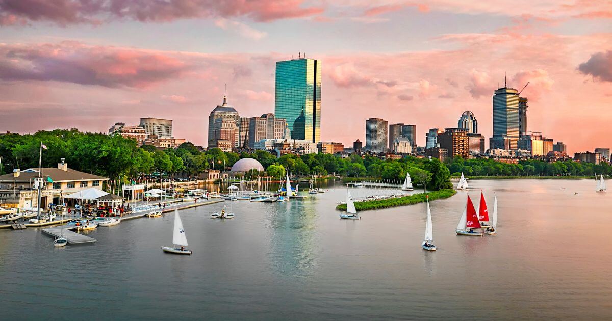 Photo of the Charles River during sunset with lots of sailboats in the foreground and the Boston skyline in the background.