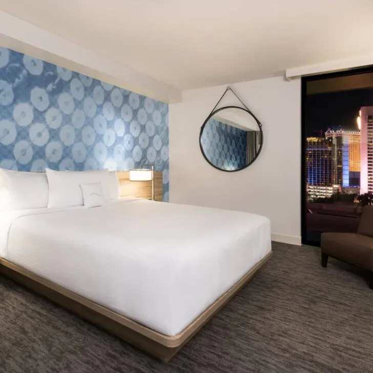 Photo of a deluxe room at the LINQ hotel with blue artwork behind the bed and a view of the strip from the window.