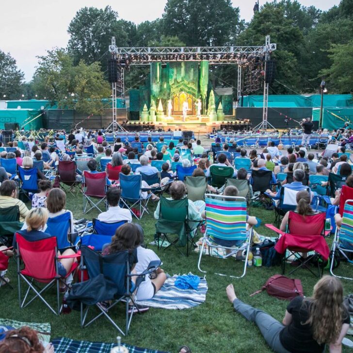 Photo of people sitting in lawn chairs on Boston Common while watching the Commonwealth Shakespeare Company perform Love's Labour's Lost on a stage.