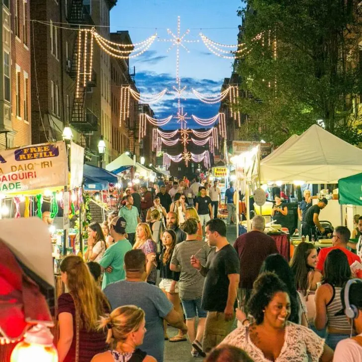 Photo of a crowd of people walking down a street in North End Boston with food and craft vendors lining both sides of the street.