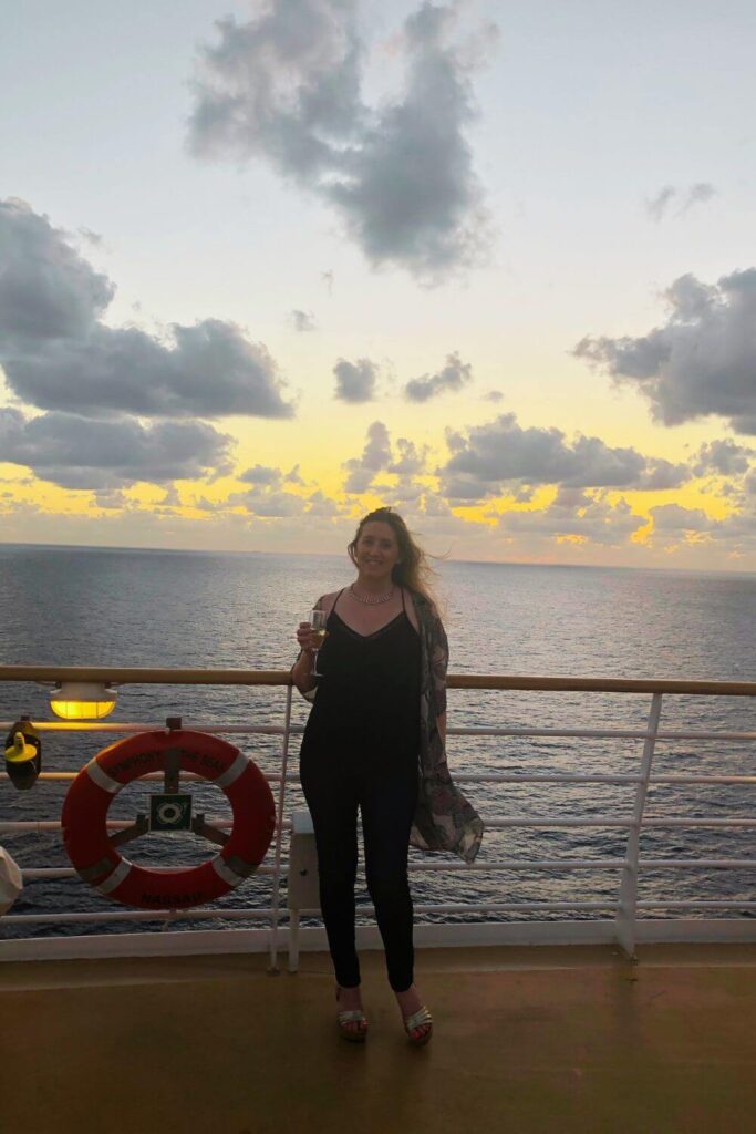 Photo of travel blogger Meg Frost posing on a cruise ship during sunset with a glass of champagne.