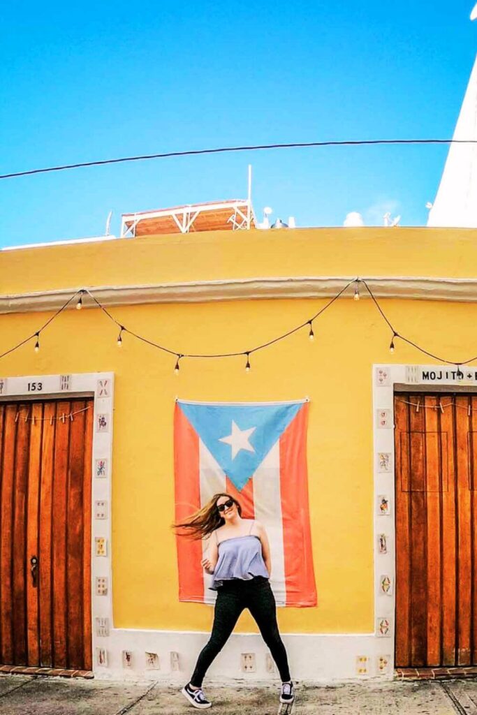 Photo of travel blogger Meg Frost dancing in front of a Puerto Rico flag in Old San Juan.