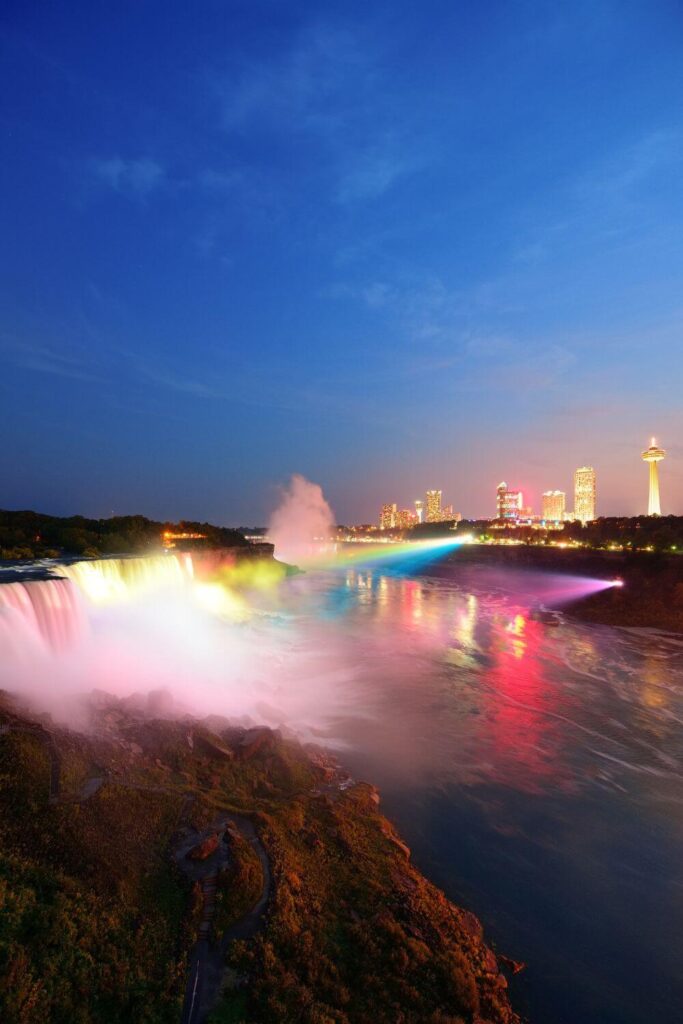 Photo of Niagara Falls at night with a colorful light projection illuminating the water in a rainbow of colors.
