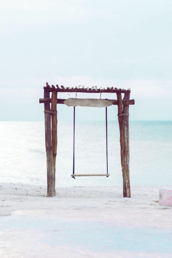 Photo of a wooden swing on a beach with the ocean in the background.