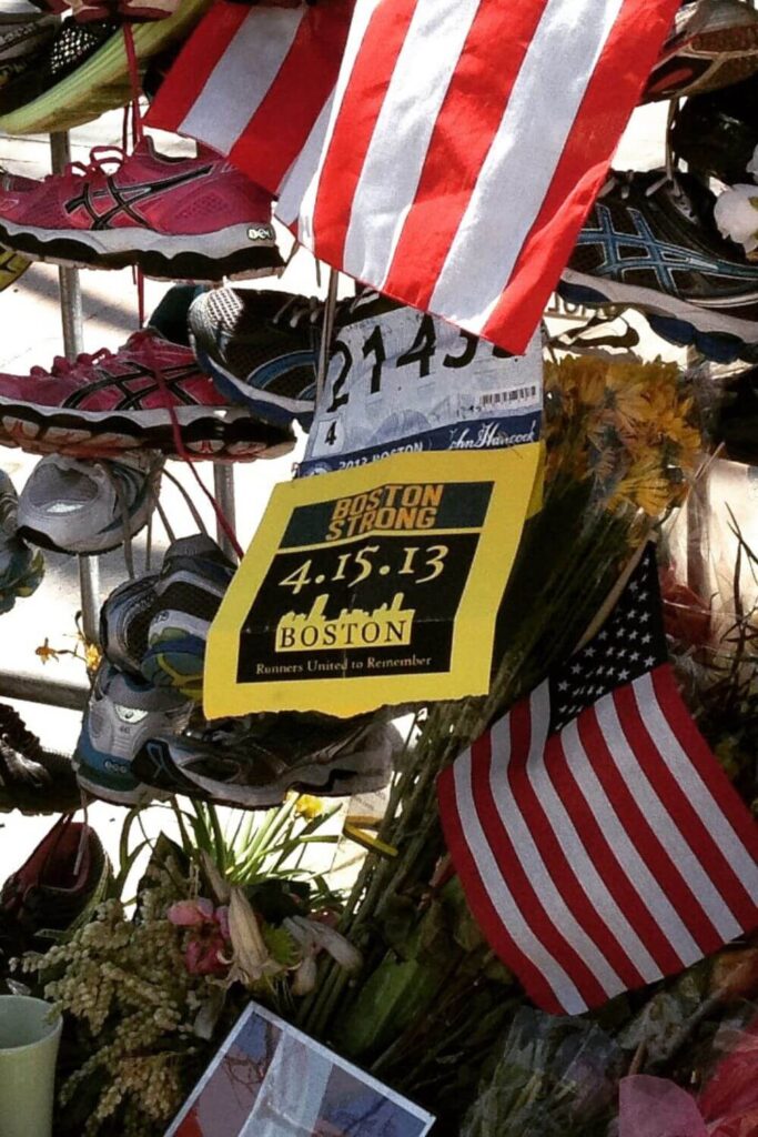Closeup of a bike rack with shoes, flowers, and flags left as a memorial for the Boston Marathon.