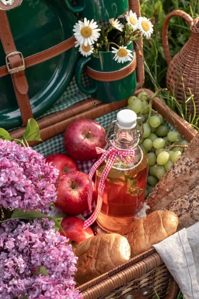 Closeup photo of a picnic basket with apples, grapes, bread, juice, and lilacs.