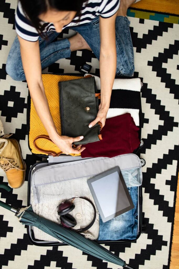 Top-down photo of a woman packing a suitcase with warm layers, like sweaters, jeans, and boots.